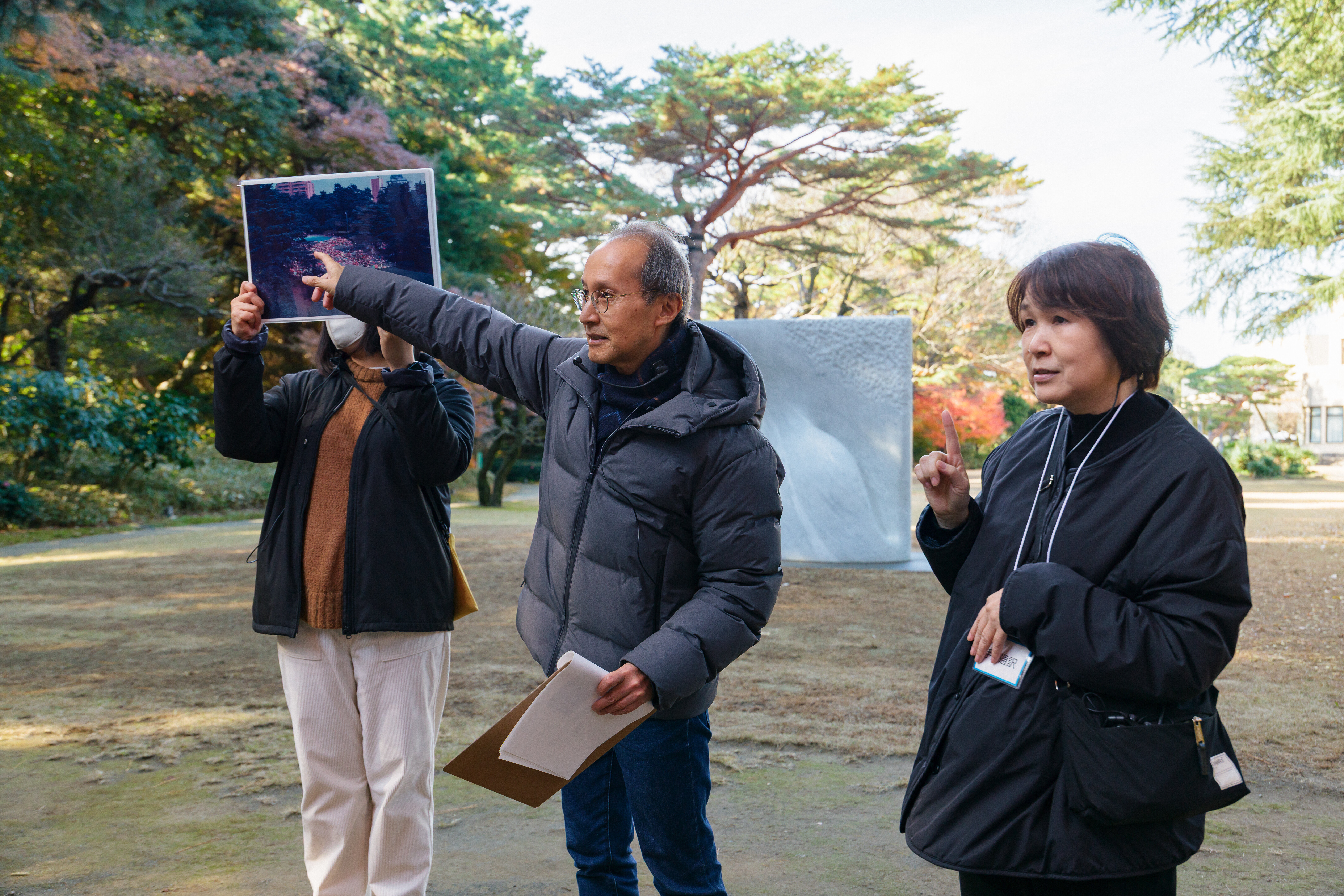 過去のツアーの様子。右手を挙げて指差しする学芸員の横には写真を掲げる女性と手話通訳をする女性が立っている。
