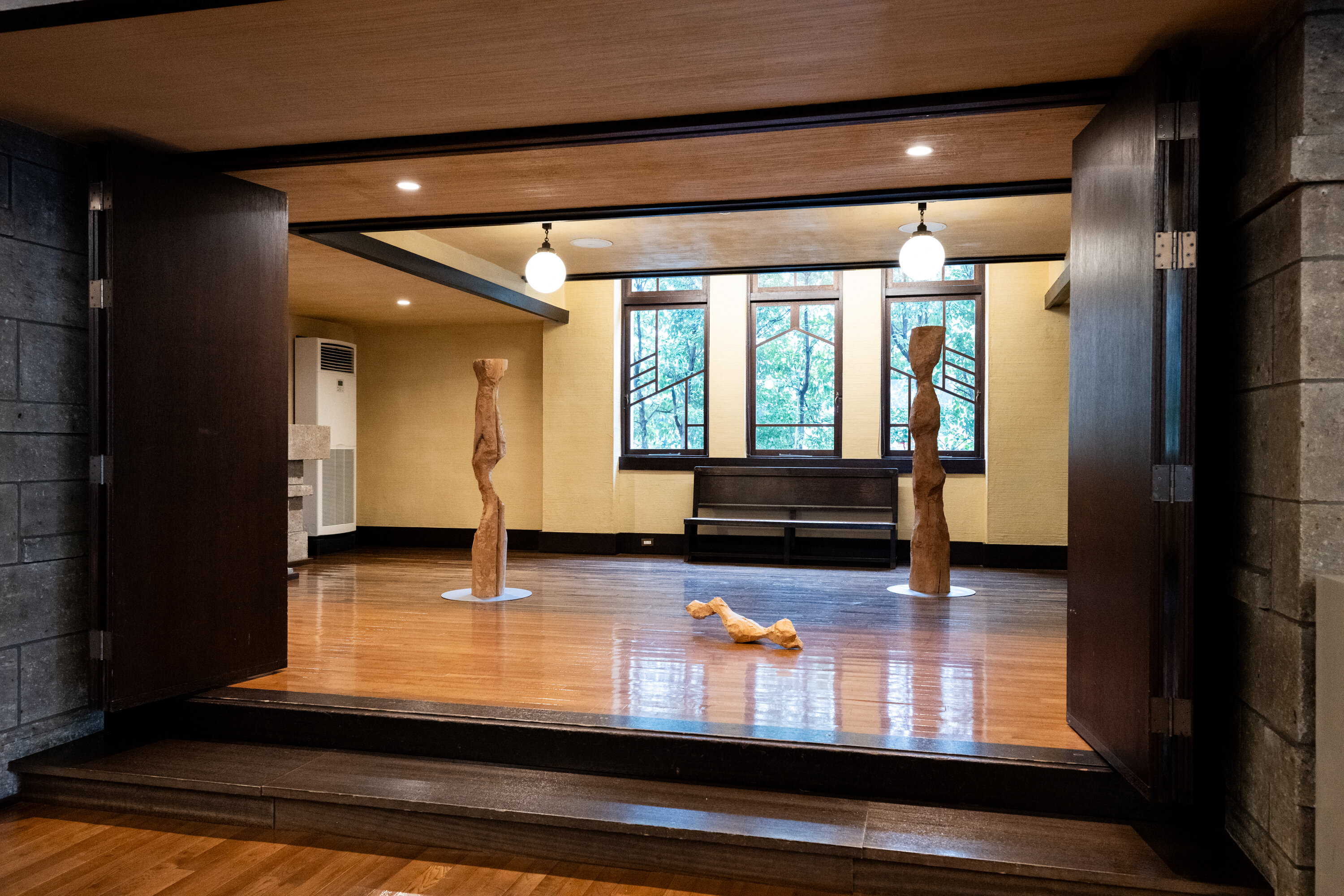 ２つの丸い照明が照らしている広間のようなところに、くねくねとした形の木のオブジェが３つ置かれている。左端と右端のオブジェは縦長で高さ１．６メートルほどで垂直に、中央手前には長さ１メートルほどのオブジェが横向きに置かれている。