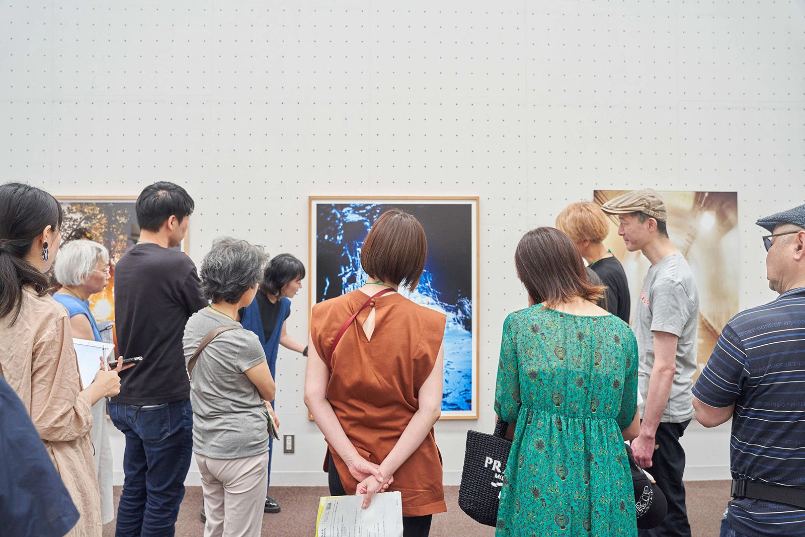 展示・ワークショップの写真。正面の壁に飾られた写真作品を囲んで10名の参加者が立って鑑賞している。