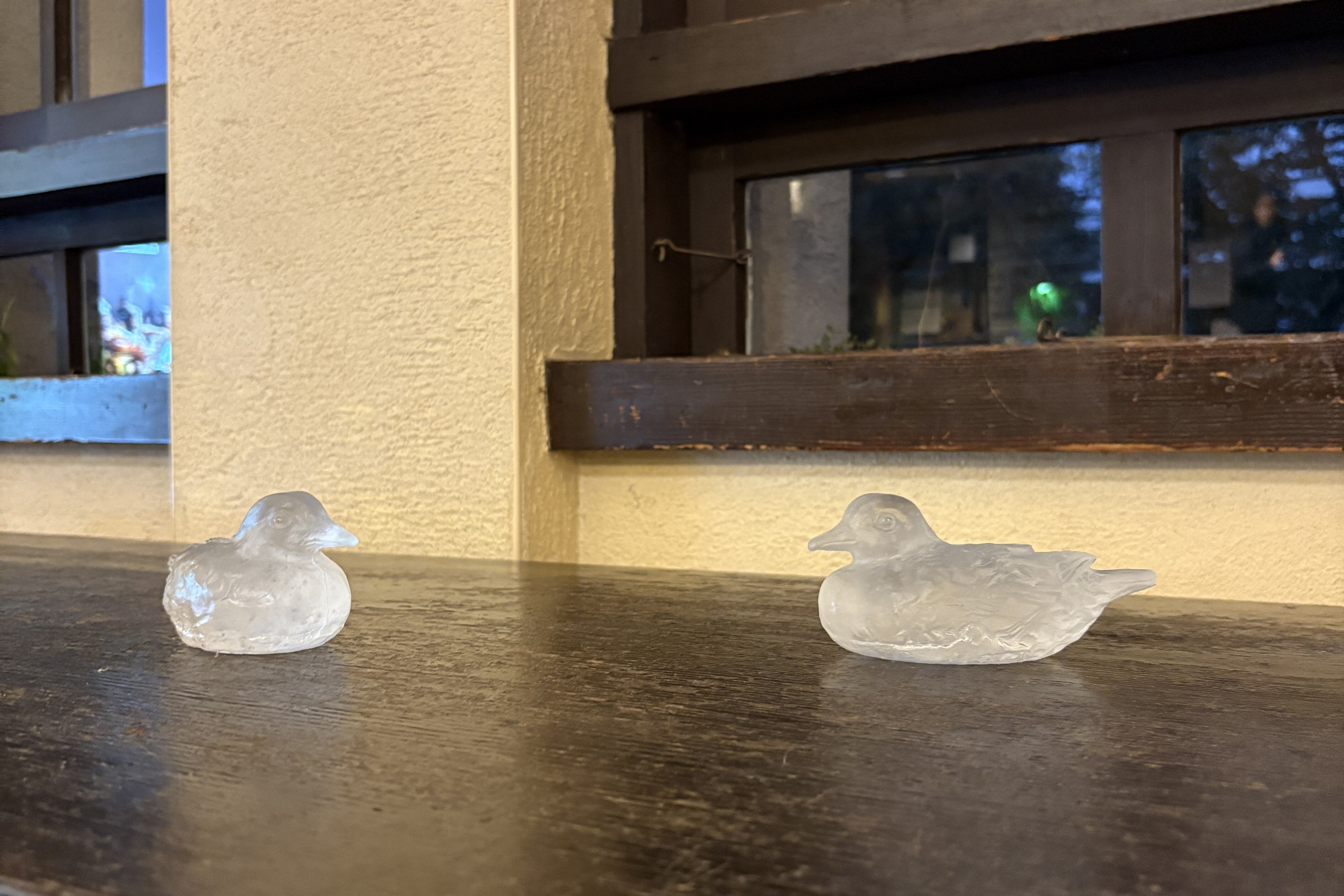 窓際にある木製の机の上に、2羽の水鳥のオブジェが互いに向かい合うような形で置かれている。オブジェは曇りガラスのような質感。