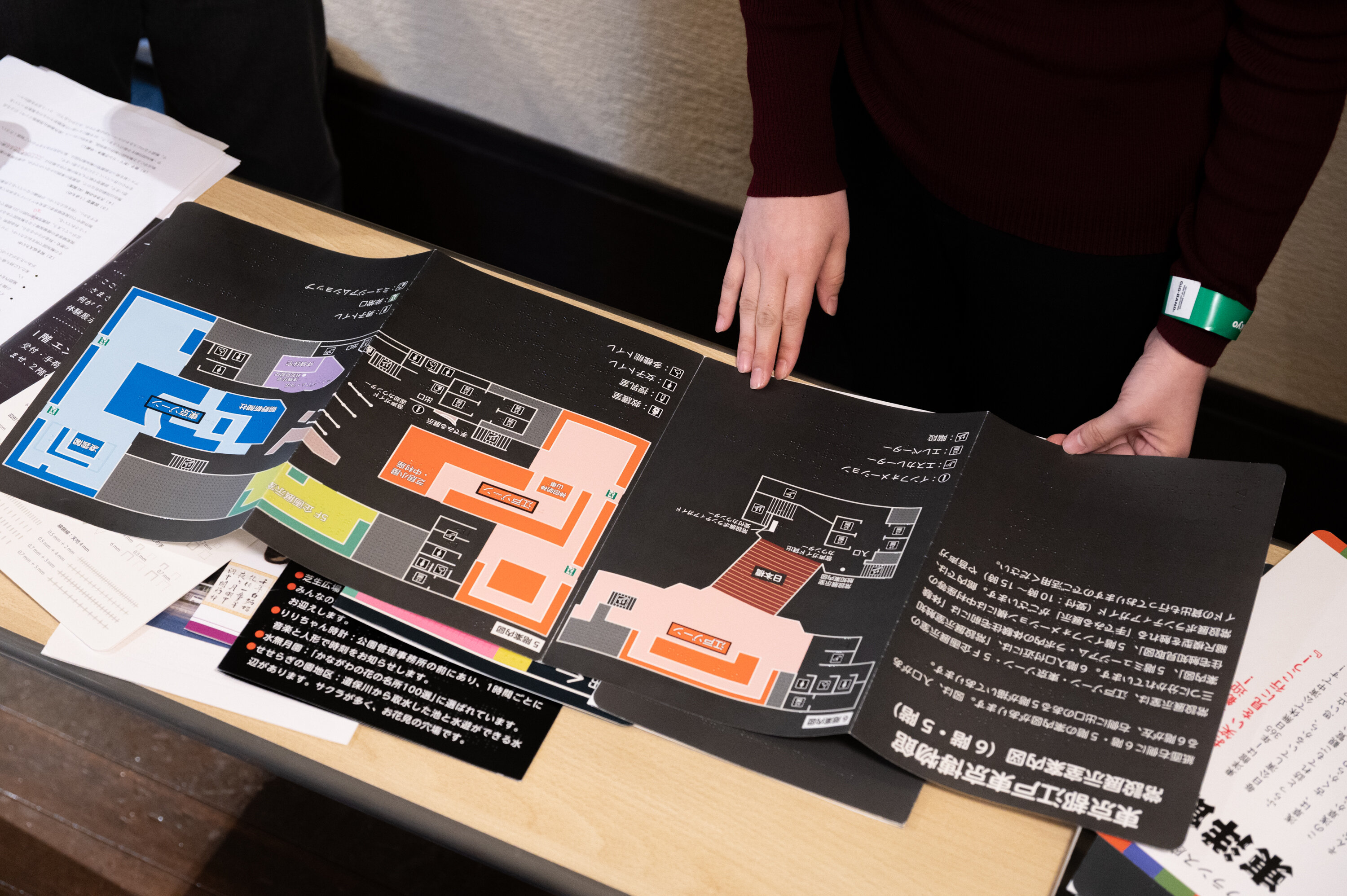 参加者が机の上で、江戸東京博物館の常設展示室触知案内図を広げ、案内図の点字を手で触れている。案内図は黒い背景に白文字のテキストと、館内図が描かれている。