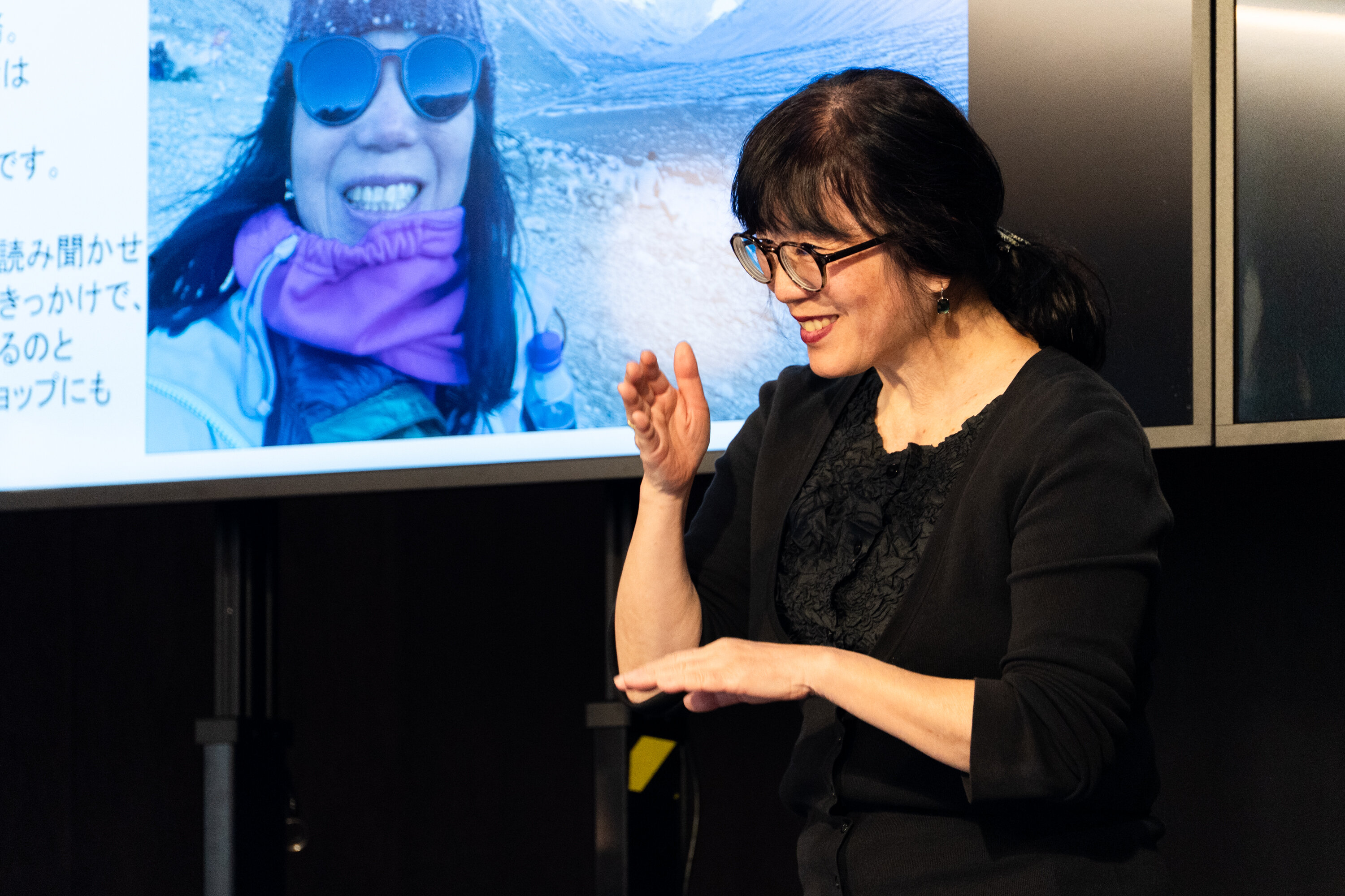 眼鏡をかけて黒い服を着た登壇者が笑顔で、手話で「ありがとう」と伝えている。