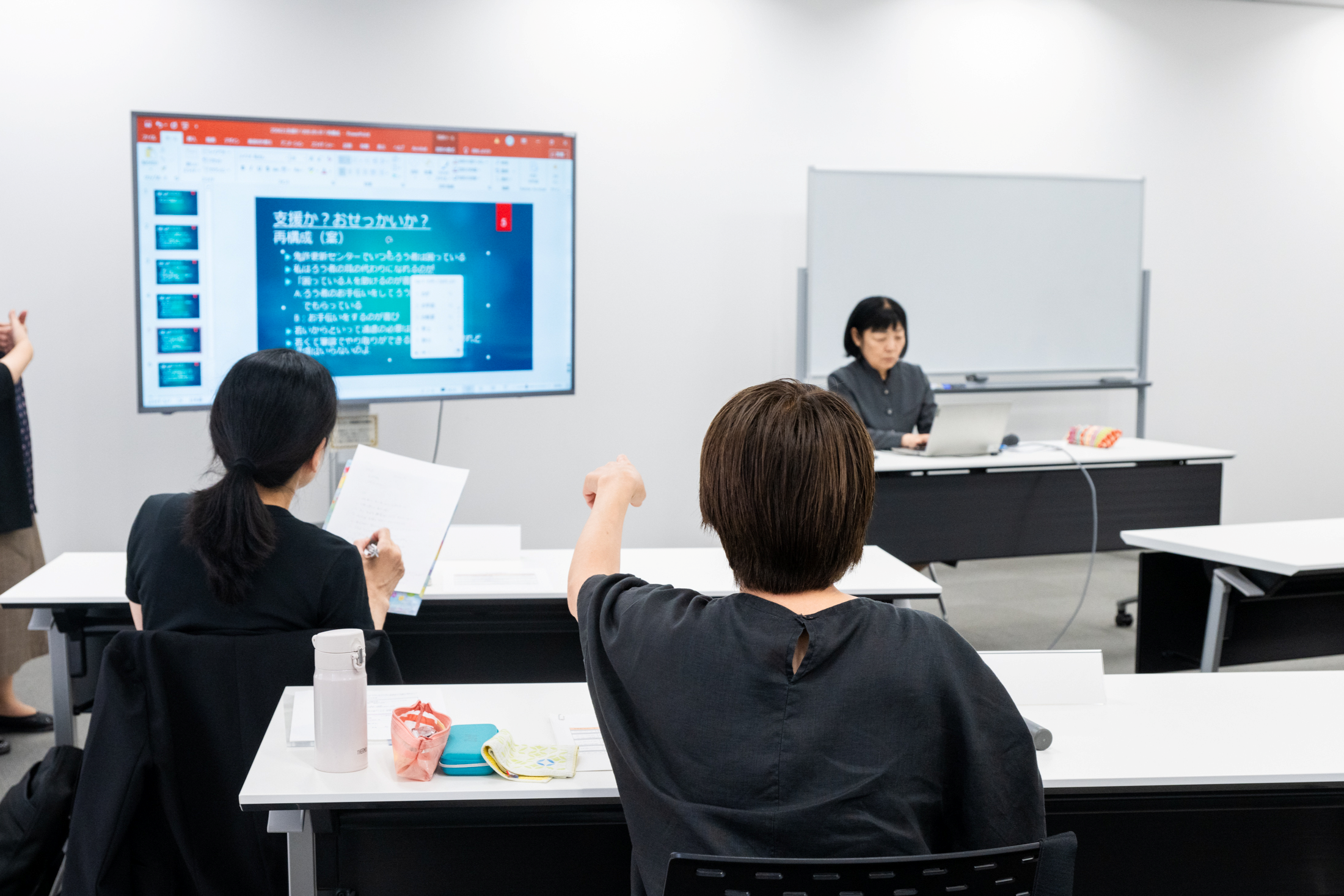 2人の生徒がメモを取ったりスライドを指さして話し合う様子。